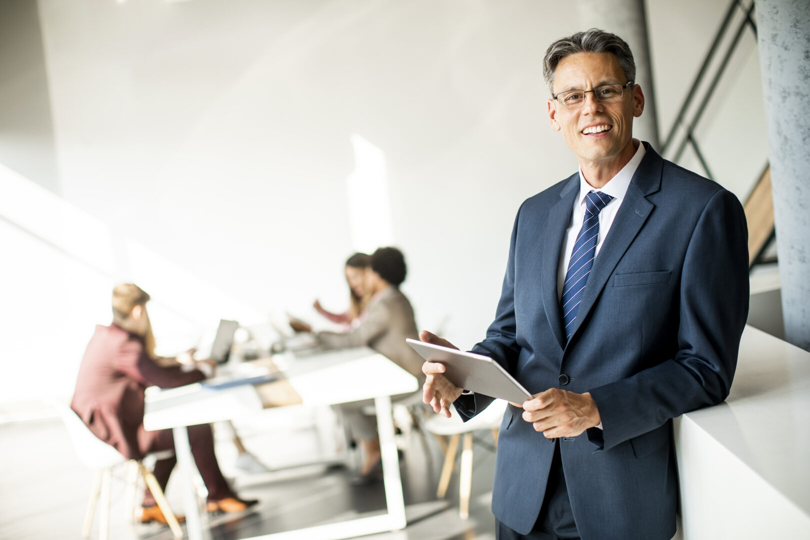 Imagen de un directivo sonriente con tablet, rodeado de un equipo de trabajo, simbolizando los beneficios de las certificaciones en inteligencia artificial en el ámbito empresarial.