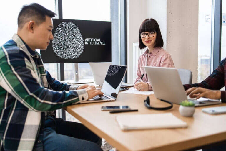 Profesionales trabajando en equipo, usando computadoras portátiles con inteligencia artificial en una oficina, discutiendo sobre la auditoría de la IA para asegurar su transparencia y desempeño ético.