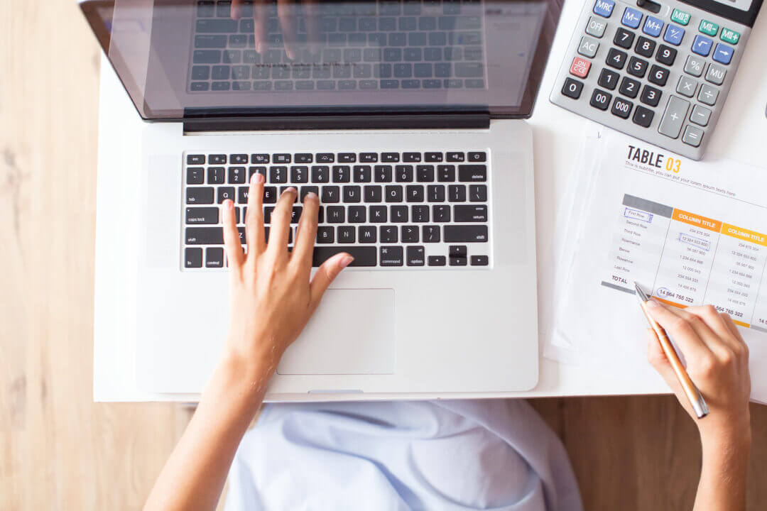 Manos sobre un portátil con hojas de cálculo y calculadora, representando la gestión del presupuesto IT en una empresa.