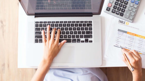 Manos sobre un portátil con hojas de cálculo y calculadora, representando la gestión del presupuesto IT en una empresa.