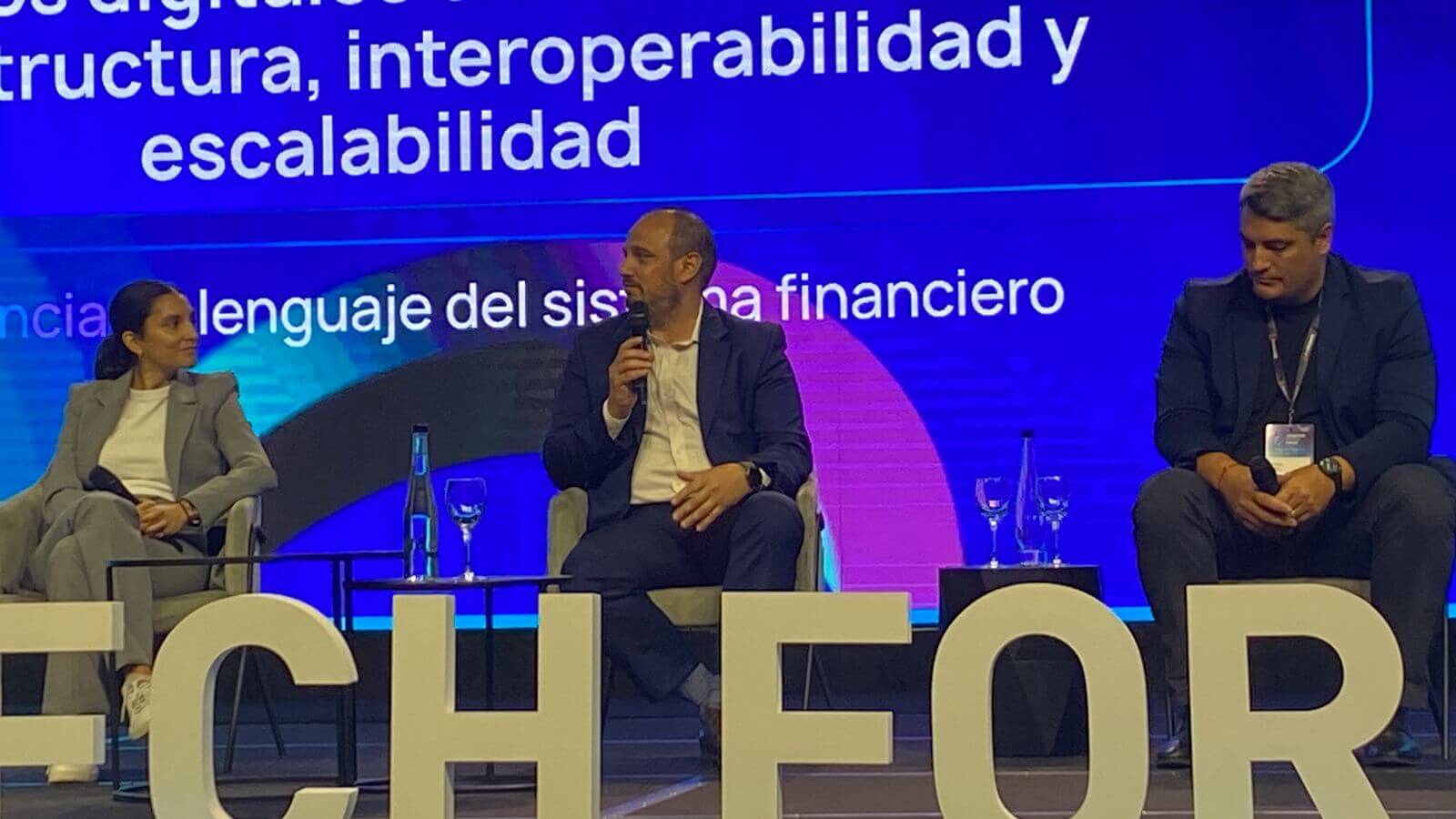 Panel de expertos en un escenario del Argentina Fintech Forum donde tres referentes debaten sobre pagos digitales frente a una pantalla con ejes temáticos.