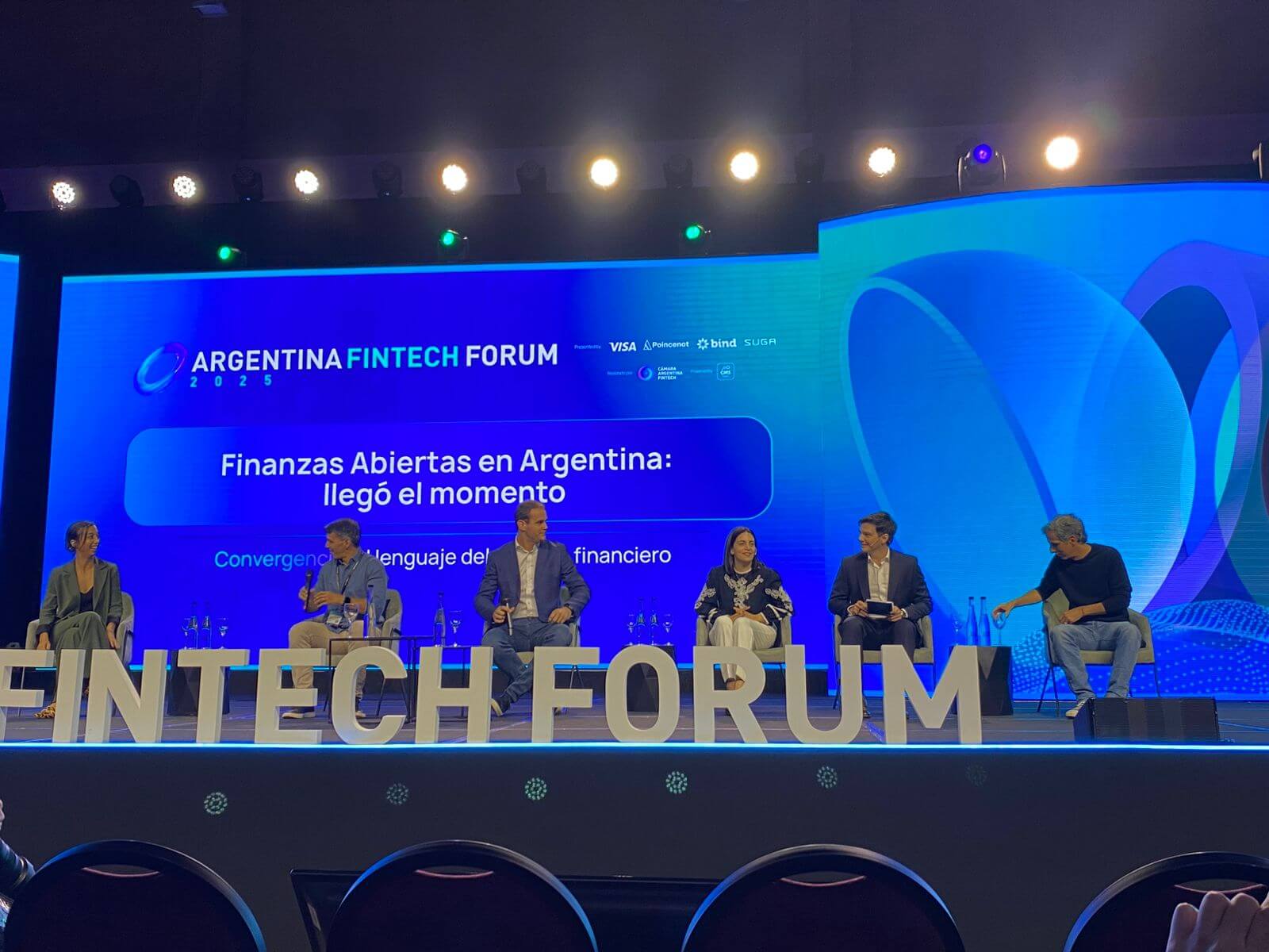 Panel de expertos en el Argentina Fintech Forum 2025 que analiza el avance del Open Finance en Argentina, con seis referentes del ecosistema sentados en el escenario frente a una pantalla institucional.