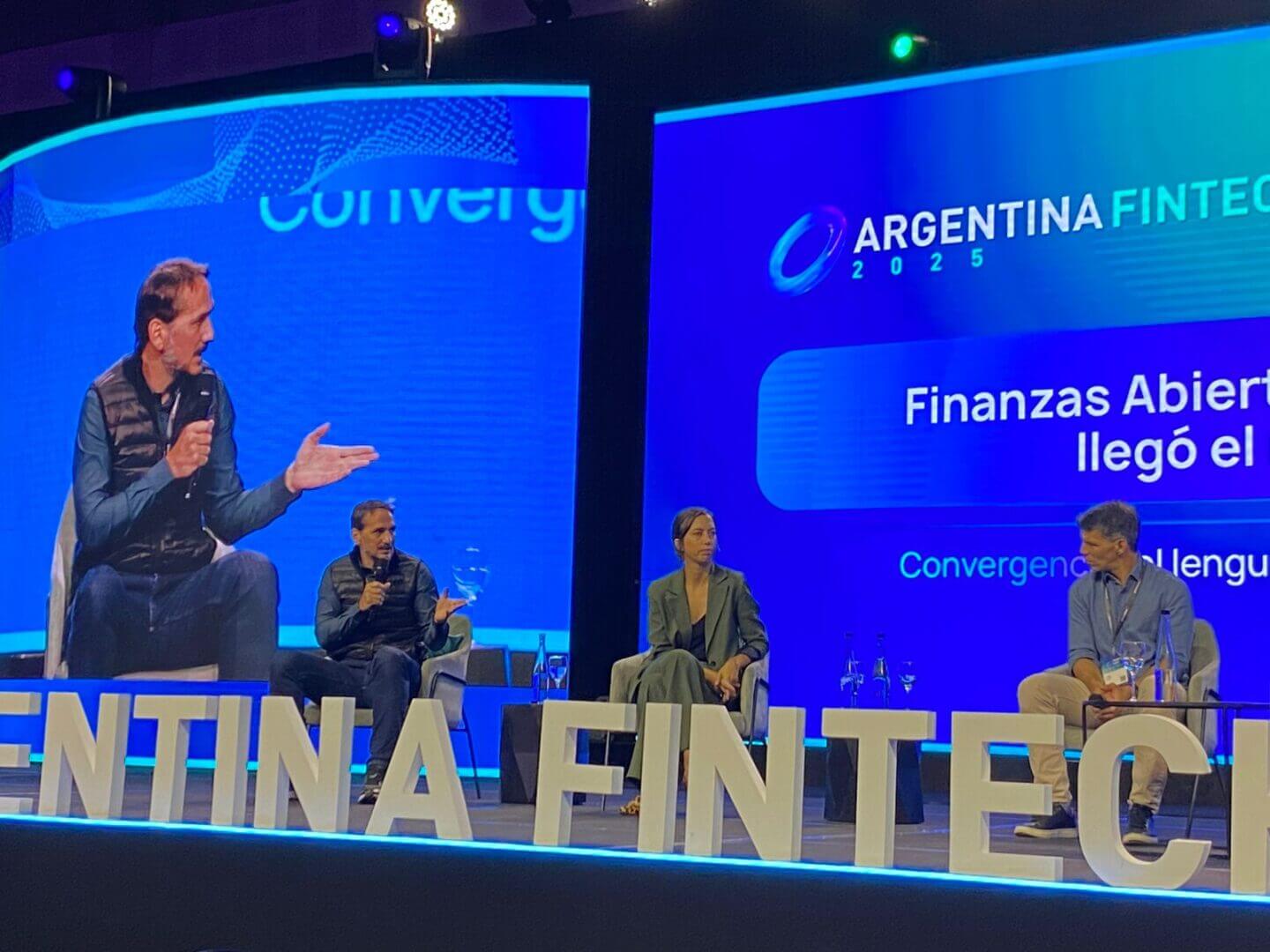 Tres referentes del ecosistema fintech sentados en el escenario del Argentina Fintech Forum 2025 mientras conversan sobre Open Finance, con una pantalla azul que muestra el eje del panel.
