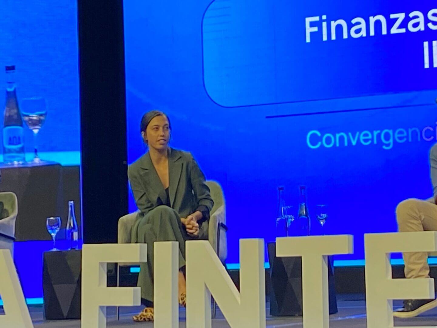 Integrante del panel del Argentina Fintech Forum 2025 sentada en el escenario durante la sesión dedicada al Open Finance, con la pantalla del evento de fondo en tonos azules.