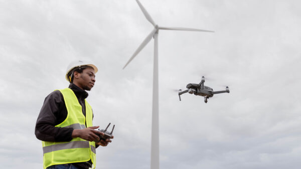 Técnico con casco y chaleco reflectante controla un dron cerca de una turbina eólica, ejemplo de uso de drones en oil & gas para inspección de activos.