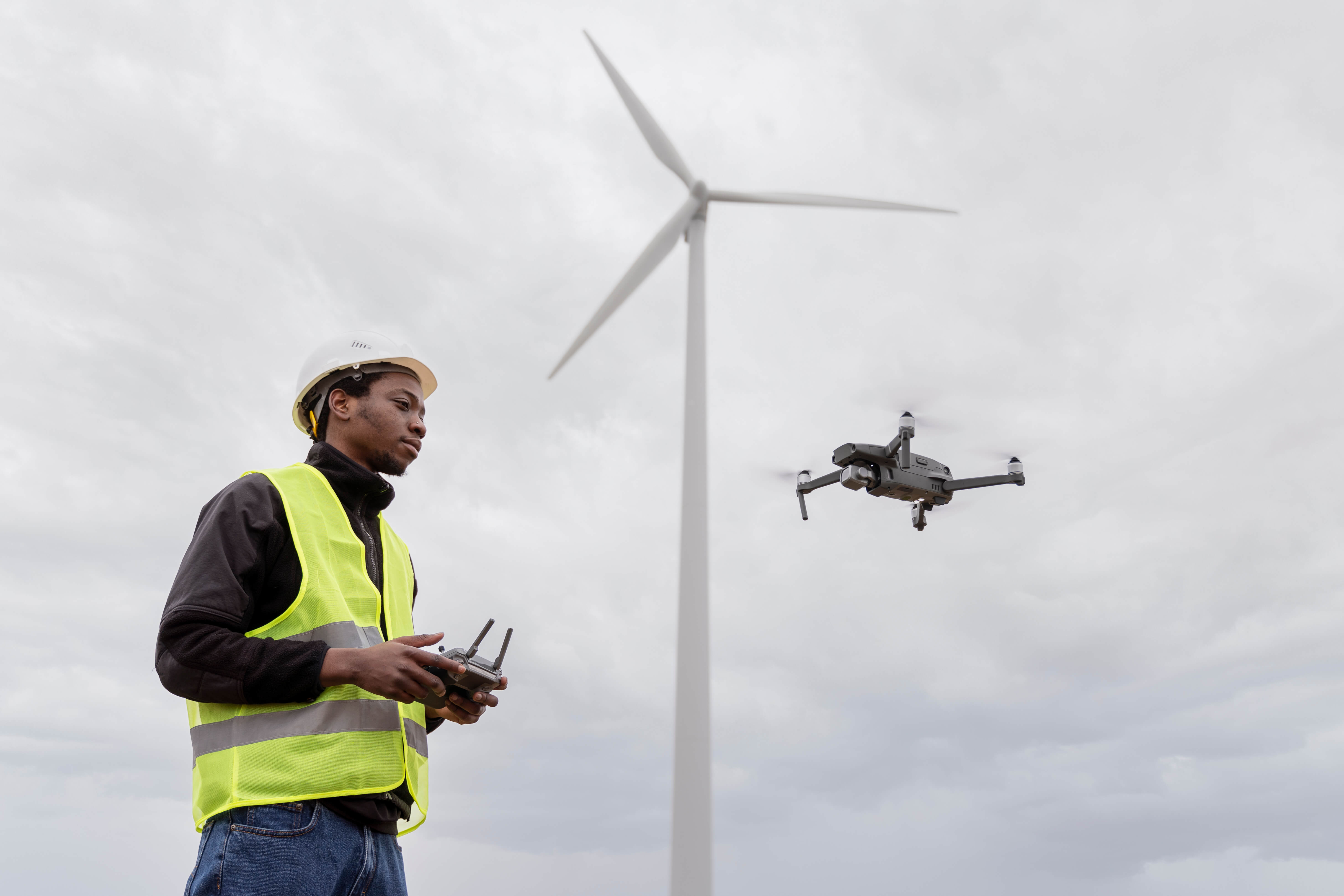 Técnico con casco y chaleco reflectante controla un dron cerca de una turbina eólica, ejemplo de uso de drones en oil & gas para inspección de activos.