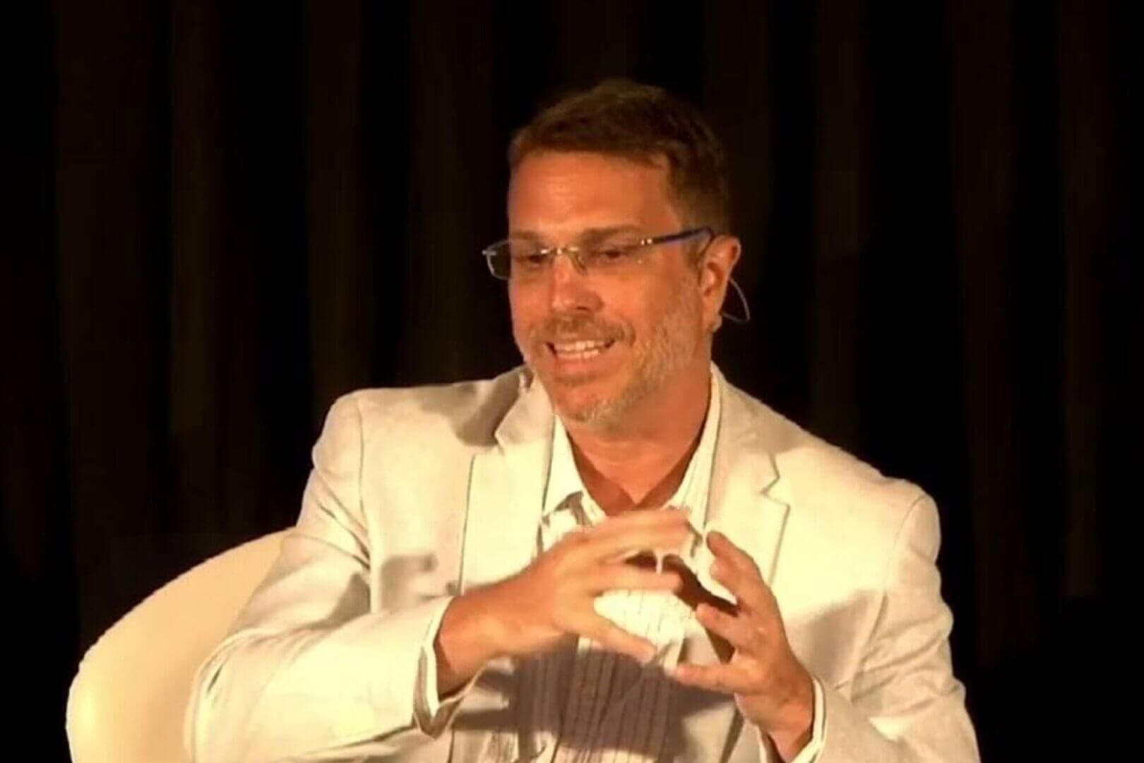 Ejecutivo de Drone AI Services en escenario, con micrófono y gesto explicativo; drones en topografia como tema central de la charla.