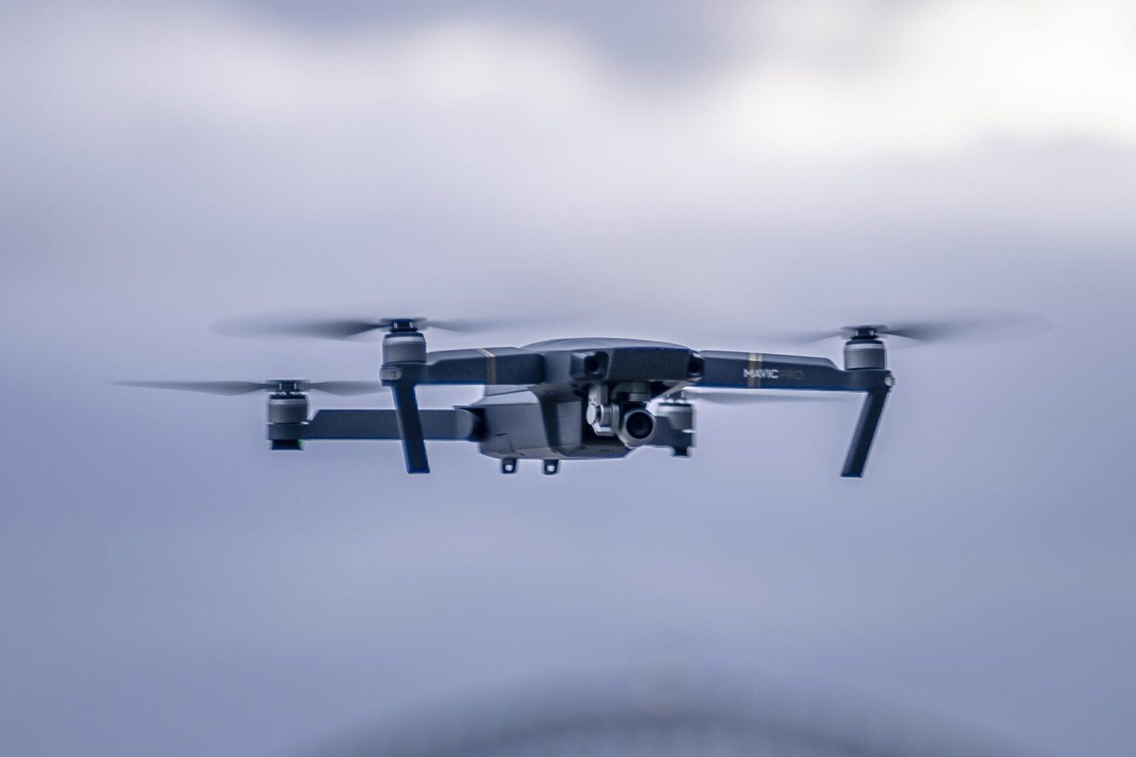 Dron cuadricóptero con cámara frontal en pleno vuelo sobre cielo nublado; drones en topografia para relevamiento y mapeo de alta precisión.