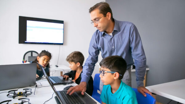 Un maestro guía a un grupo de estudiantes mientras trabajan en computadoras, destacando la importancia de la ciberseguridad en plataformas educativas.