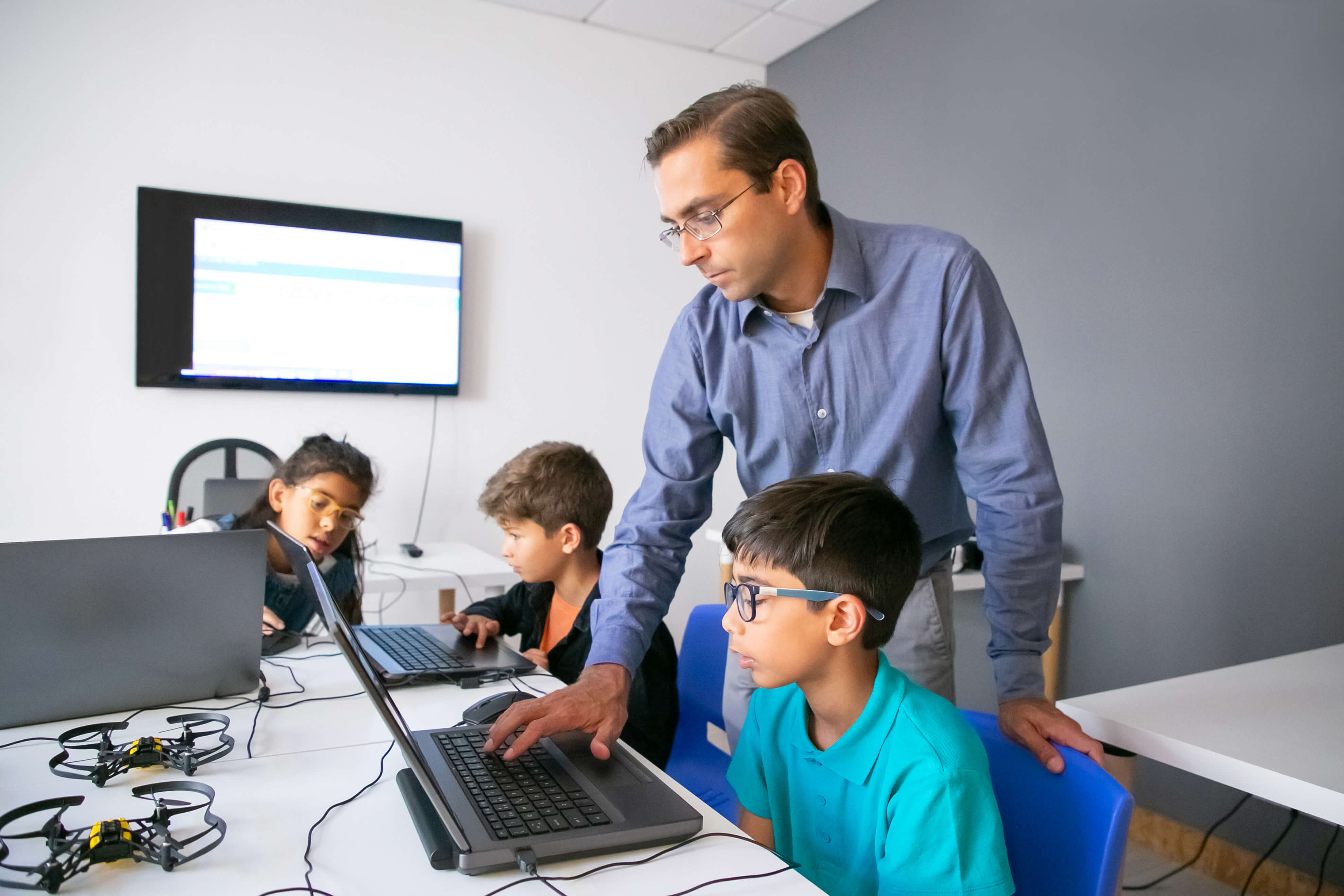 Un maestro guía a un grupo de estudiantes mientras trabajan en computadoras, destacando la importancia de la ciberseguridad en plataformas educativas.