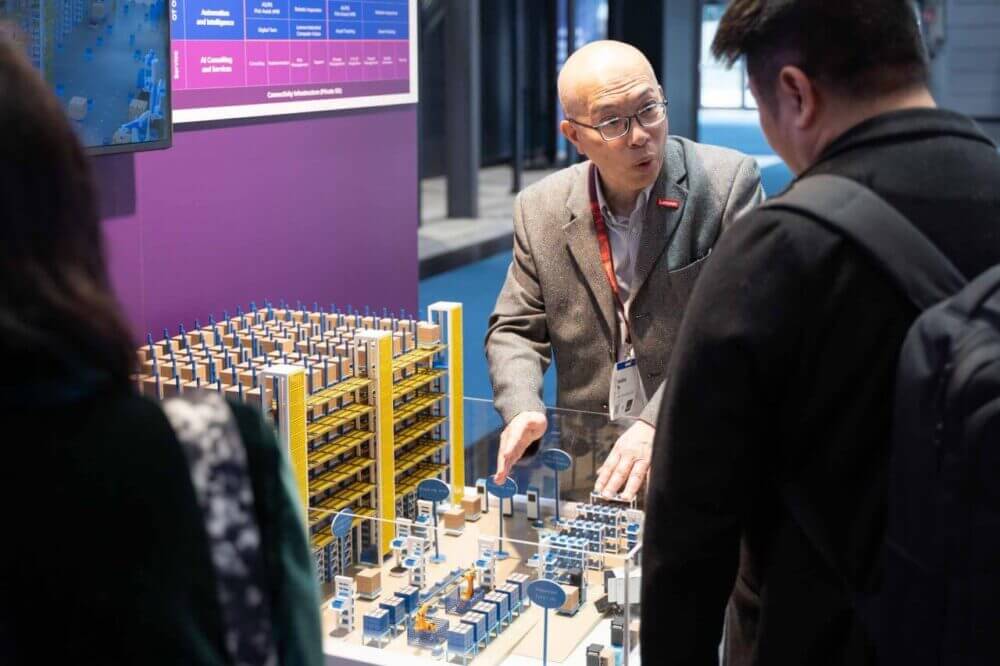 Ejecutivo explica una maqueta de fábrica inteligente en el stand de Lenovo, vinculada con IA industrial, automatización y optimización de procesos.