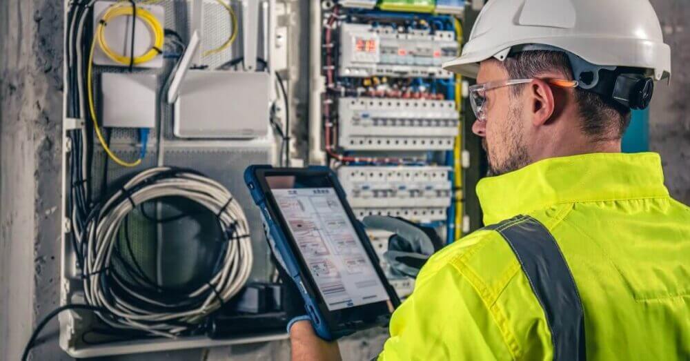 Técnico con casco revisa una tablet frente a un tablero eléctrico como parte de la operación energética basada en datos.