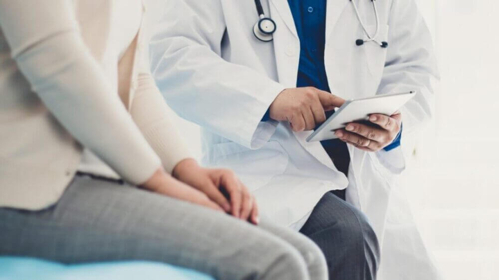 Médico usa una tablet durante una consulta con una paciente, ilustrando cómo Patient 360 ayuda a integrar datos para decisiones clínicas más confiables.