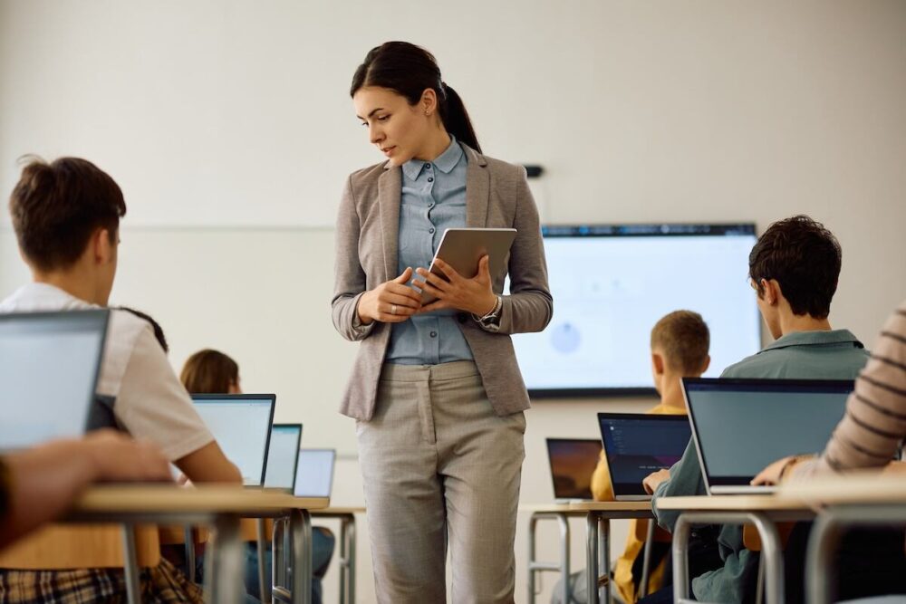 Docente observa a estudiantes con computadoras en un aula, en una escena vinculada al uso de learning analytics en educación.