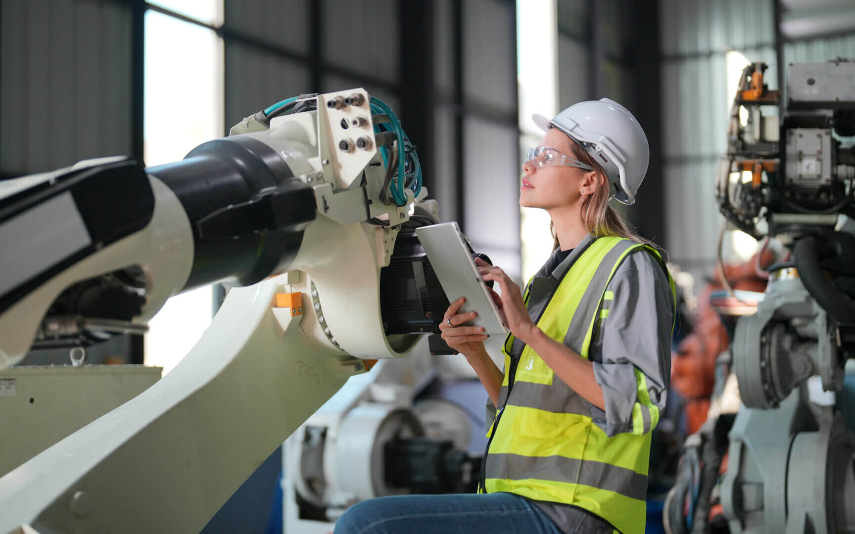 Operaria con casco y tablet revisa maquinaria industrial, una escena que representa el uso de calidad predictiva para anticipar fallas en producción.