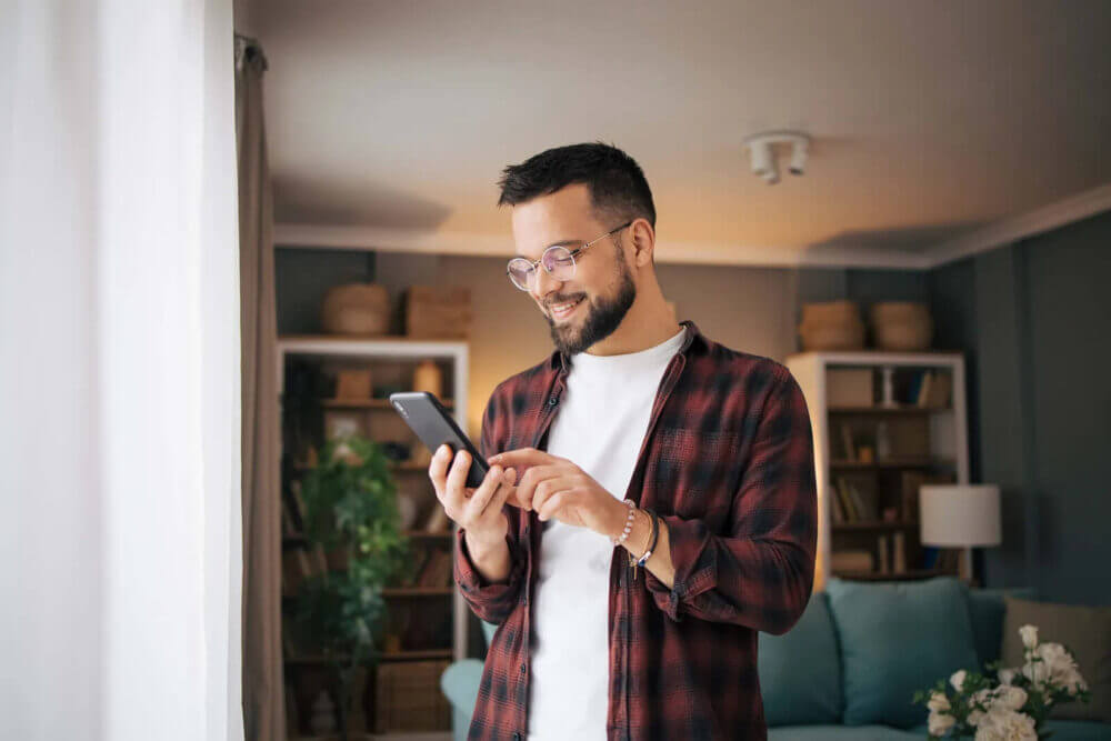 Hombre usa un teléfono móvil en su casa, en una imagen sobre IA agéntica en seguros aplicada a reclamos y atención digital.