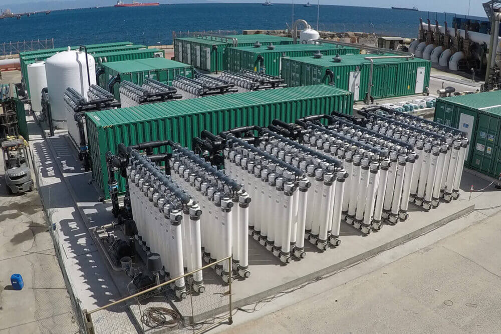 Planta industrial con módulos, tuberías y equipos de proceso junto al mar, vinculada al control avanzado de procesos en entornos industriales.