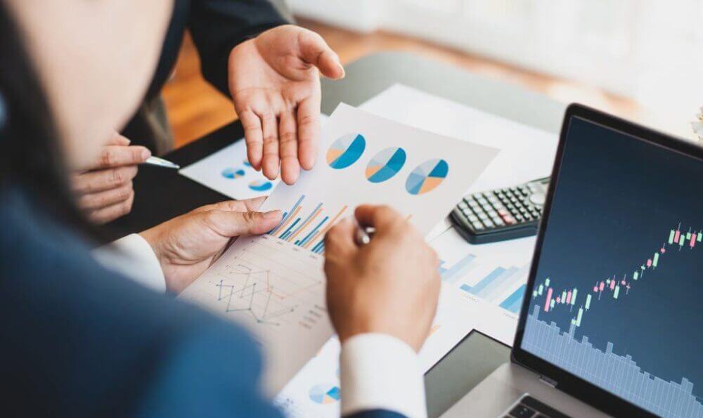 Ejecutivos analizan gráficos financieros y datos de mercado, en una escena vinculada a portfolio analytics en real estate para decisiones de inversión.