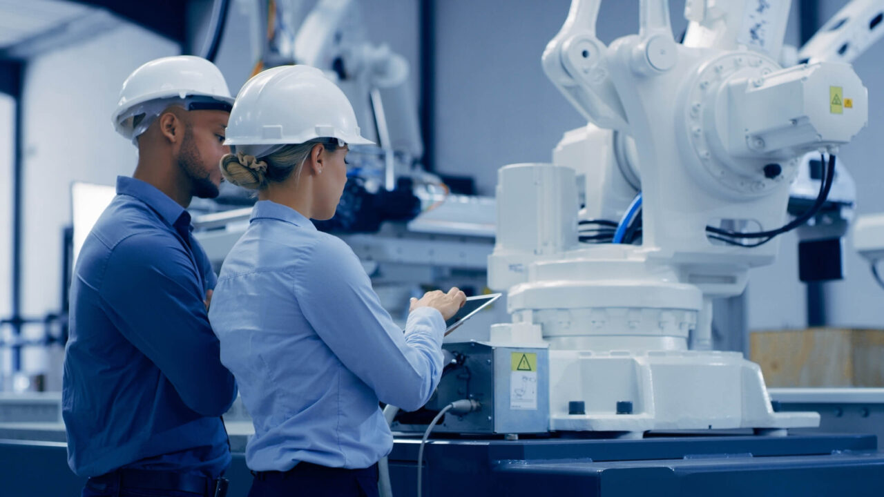 Dos profesionales observan un robot industrial en una fábrica inteligente como parte de un entorno de Educación 4.0 aplicada.
