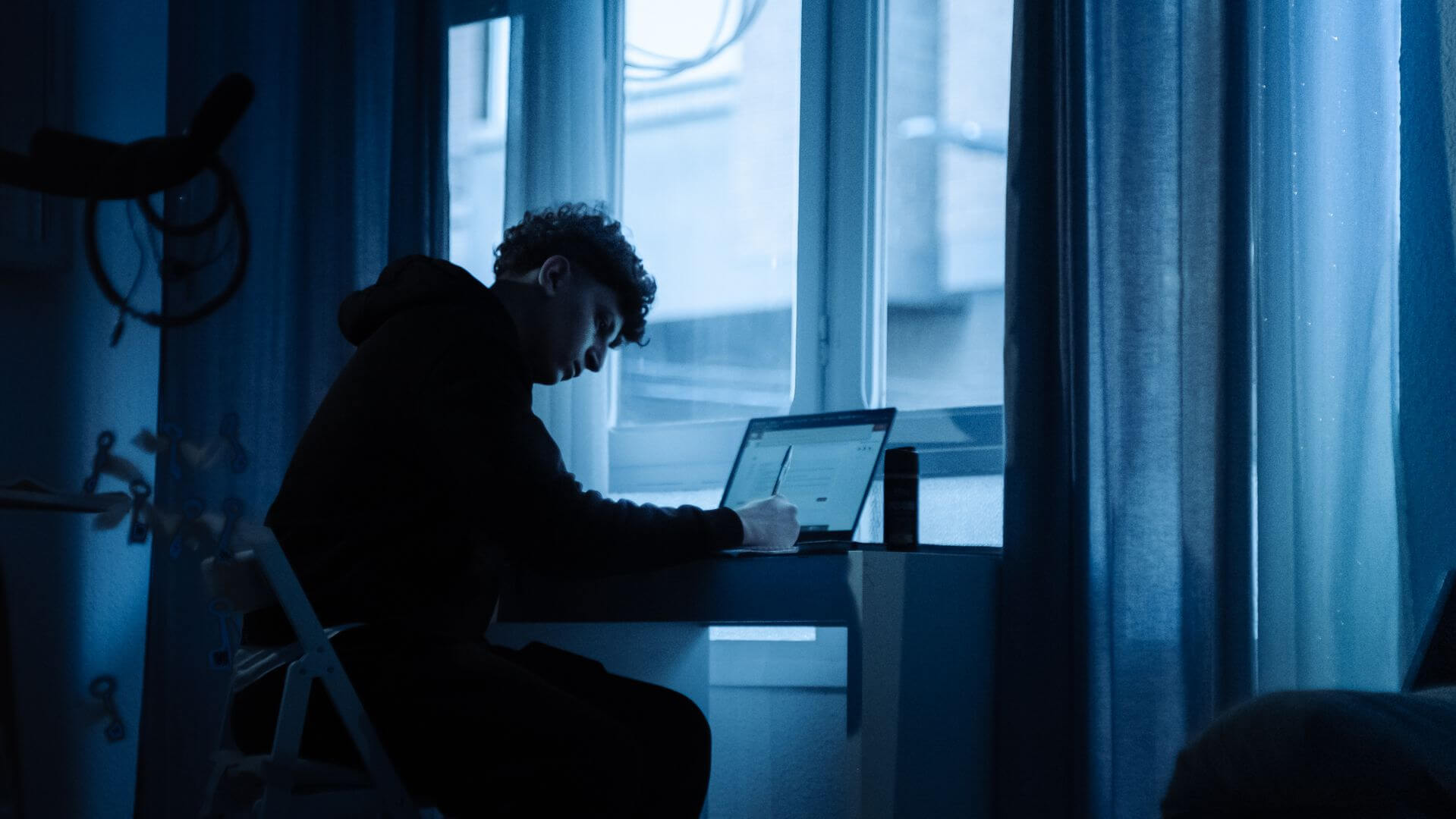Persona frente a una computadora portátil en una habitación con luz azul.