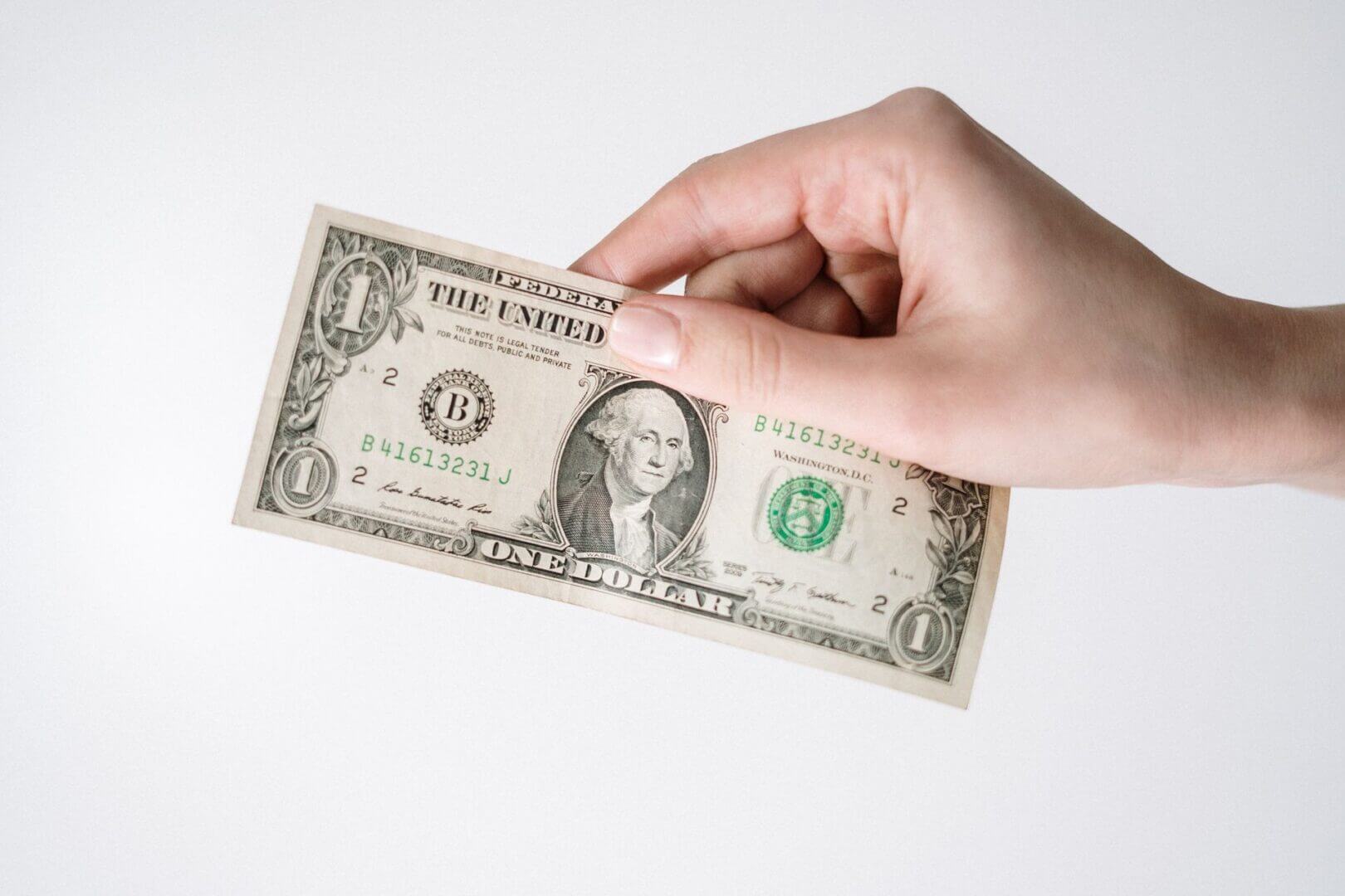 Mano que sostiene un billete de un dólar sobre fondo blanco.