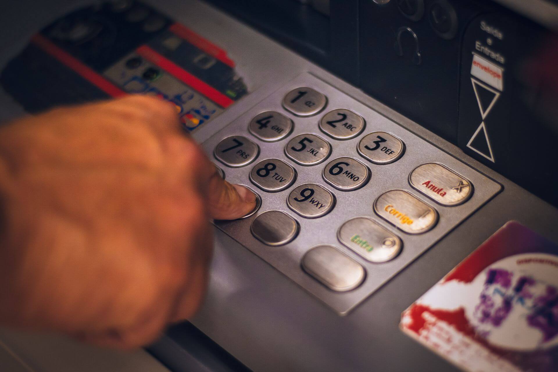 Primer plano de una persona ingresando datos en el teclado de un cajero automático con una tarjeta bancaria insertada.