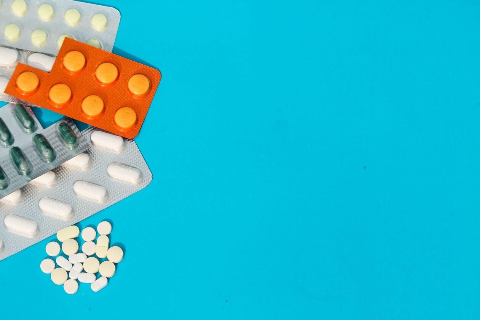 Blísteres de medicamentos y pastillas sobre un fondo celeste, imagen asociada a farmacias, salud digital y pagos embebidos.