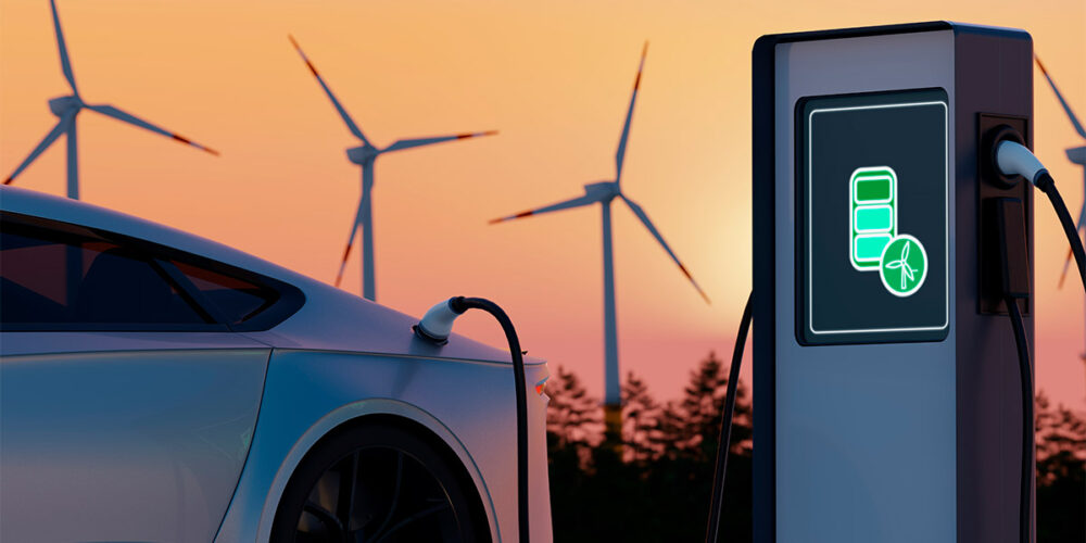 Auto eléctrico cargando en una estación con molinos eólicos al fondo, una nueva demanda para la red eléctrica.