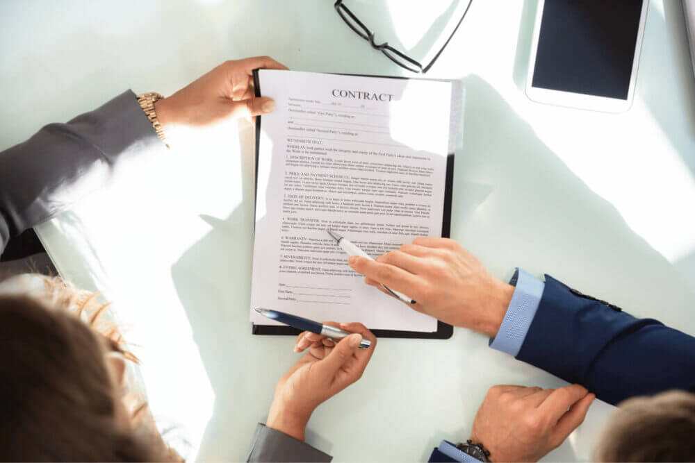 Dos profesionales revisan un contrato impreso sobre una mesa, escena vinculada al uso de contract analytics para analizar acuerdos y detectar riesgos.