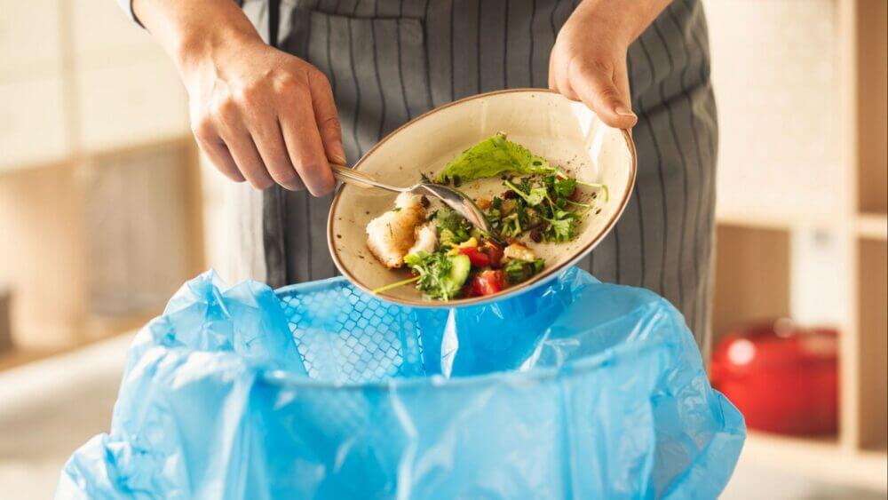 Trabajador de cocina descartando restos de comida en un contenedor, una de las pérdidas que la IA predictiva busca reducir.