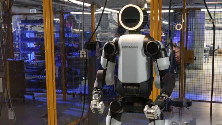 Robot humanoide de Boston Dynamics en un laboratorio de pruebas, con estructura blanca y negra detrás de una barrera de seguridad.