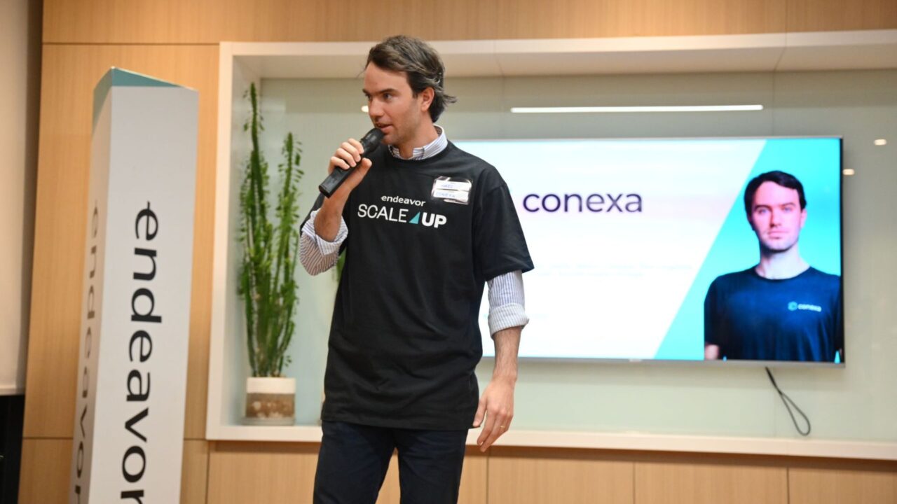 Ejecutivo de Conexa durante una exposición de Endeavor ScaleUp, con la marca de la startup en pantalla.