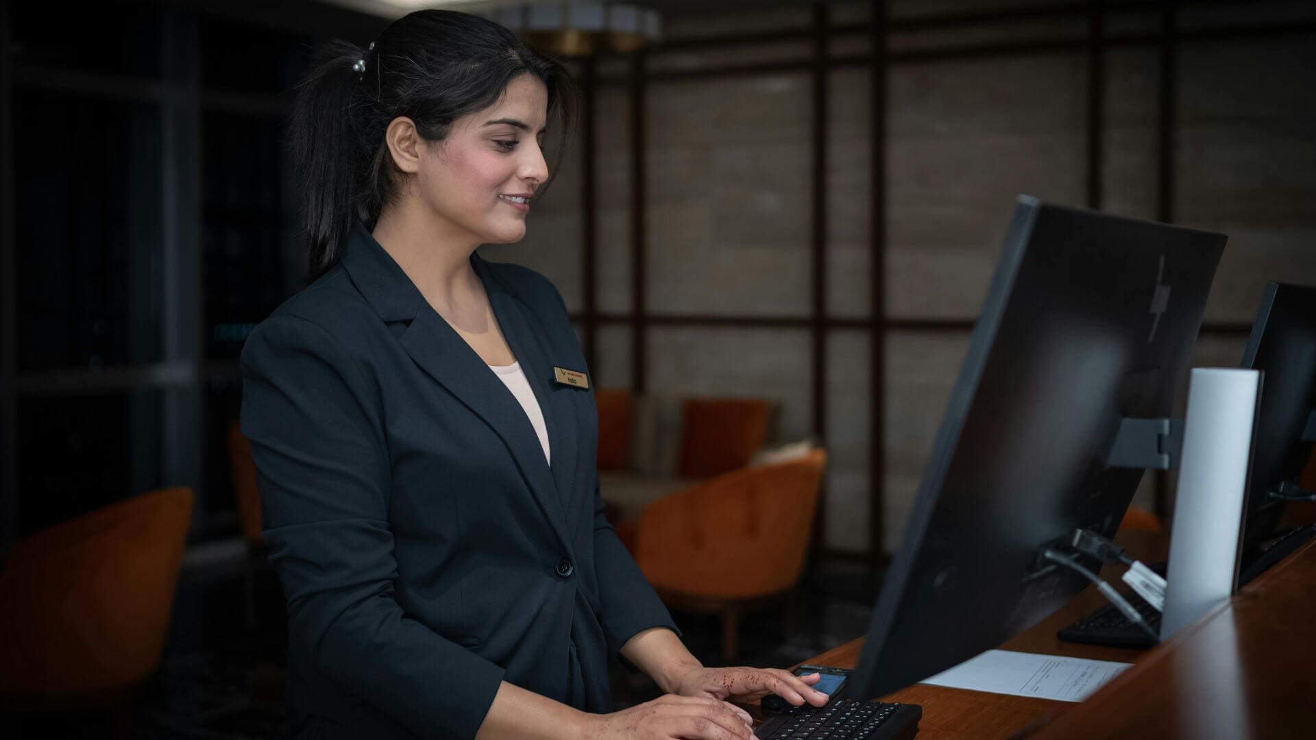 Recepcionista de hotel trabaja frente a una computadora en el área de atención al huésped.