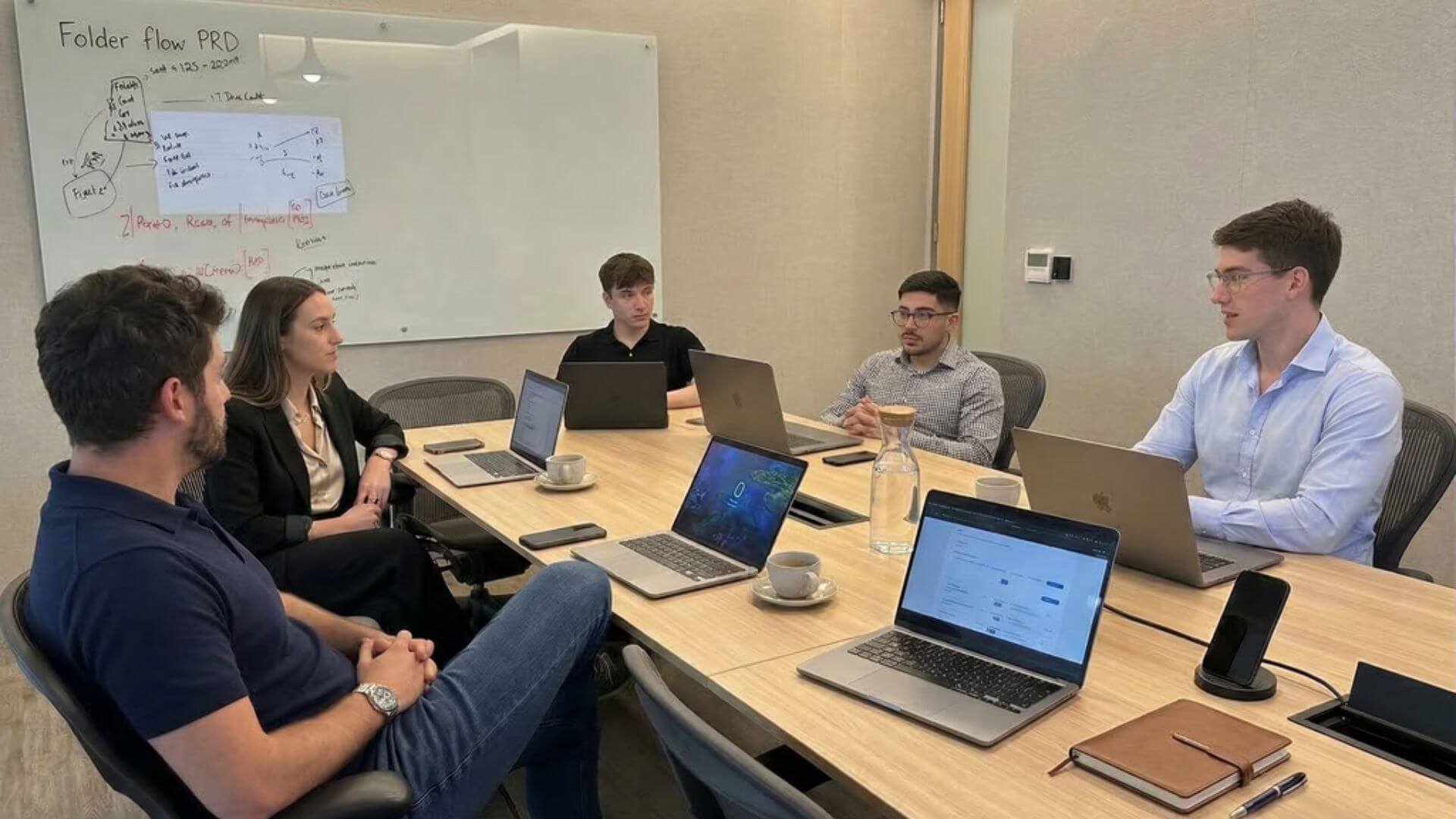 Integrantes del equipo de Fonder reunidos alrededor de una mesa con computadoras portátiles y una pizarra con esquemas de producto.