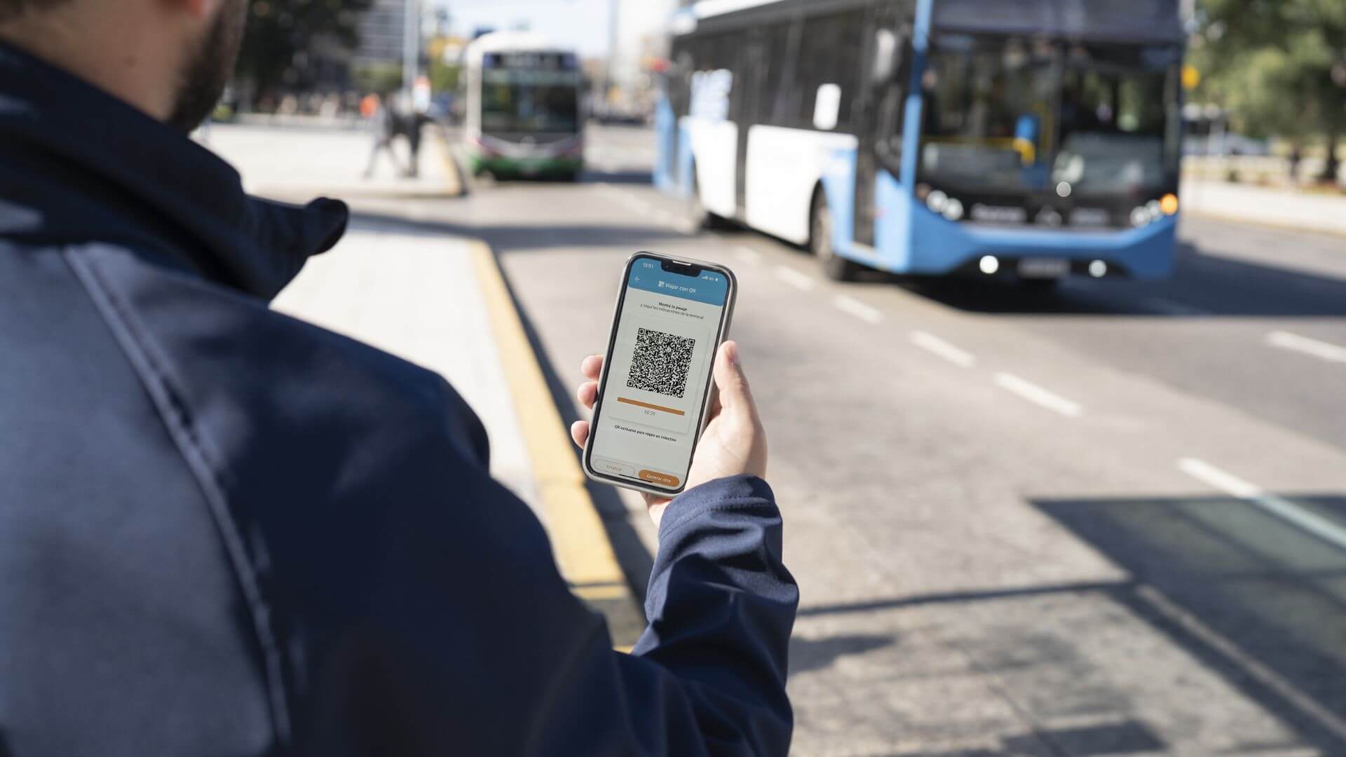 Pasajero sostiene un celular con un código QR en tranporte público mientras espera la llegada de un colectivo.