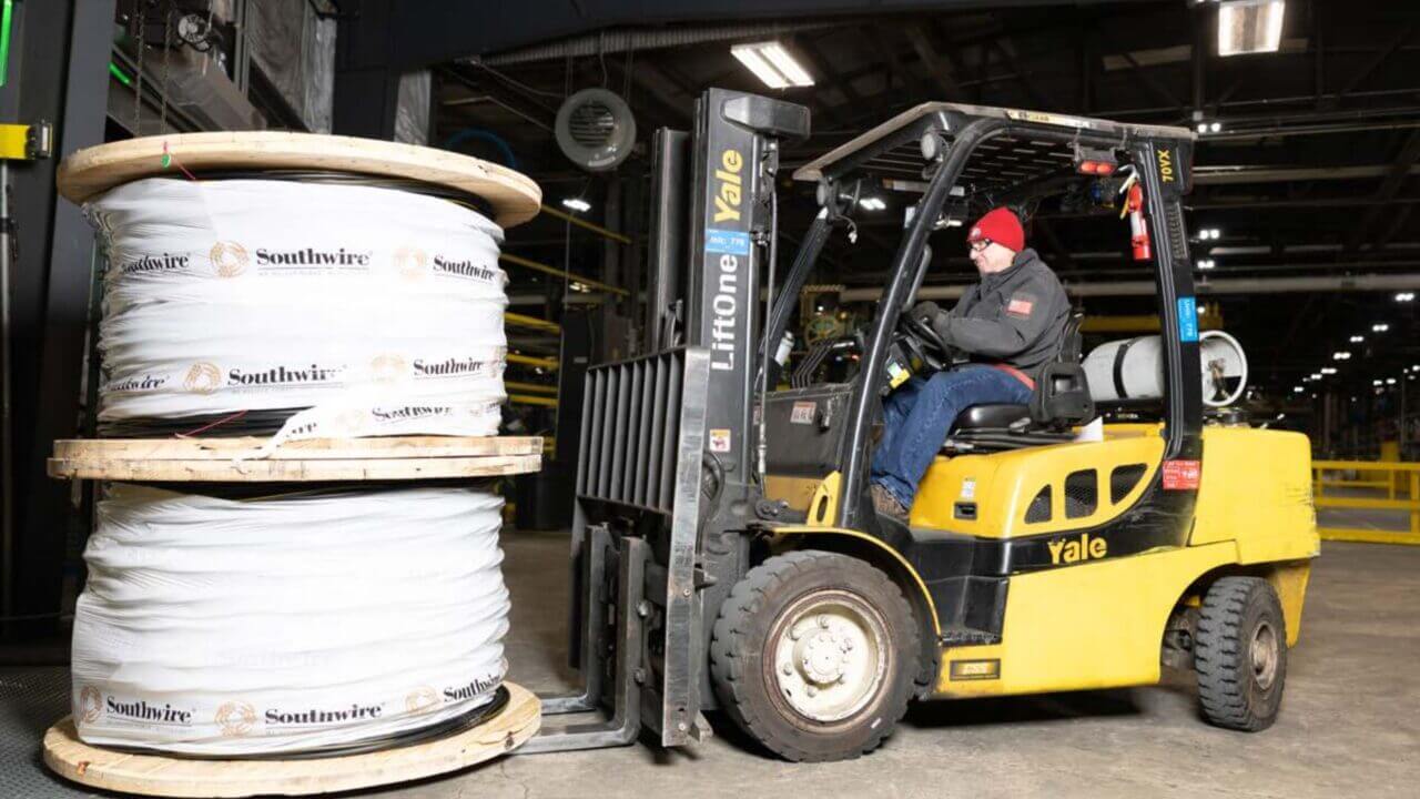 Un operario en un montacargas transporta una gran bobina de cable con el logo de southwire dentro de una planta industrial.