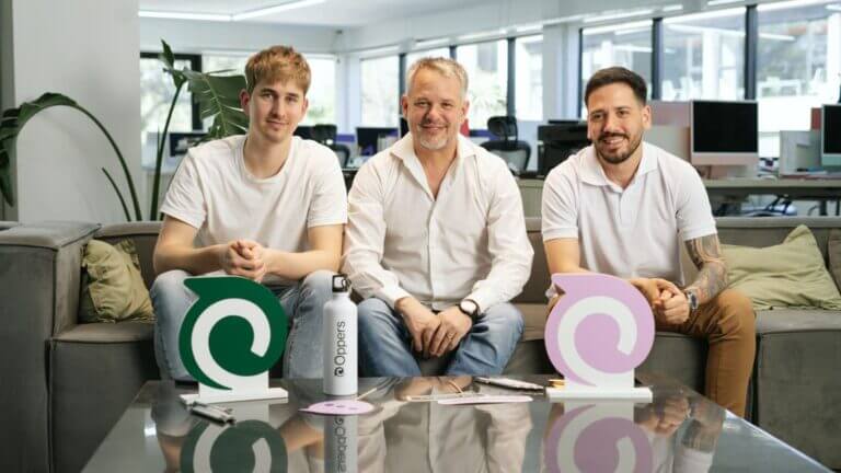 Tres fundadores de Oppers sentados en una oficina junto a elementos con el logo de la empresa.