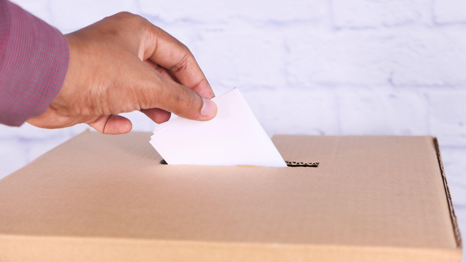 Mano introduce un voto en una urna electoral, una escena vinculada al uso de Oppers para anticipar resultados electorales.