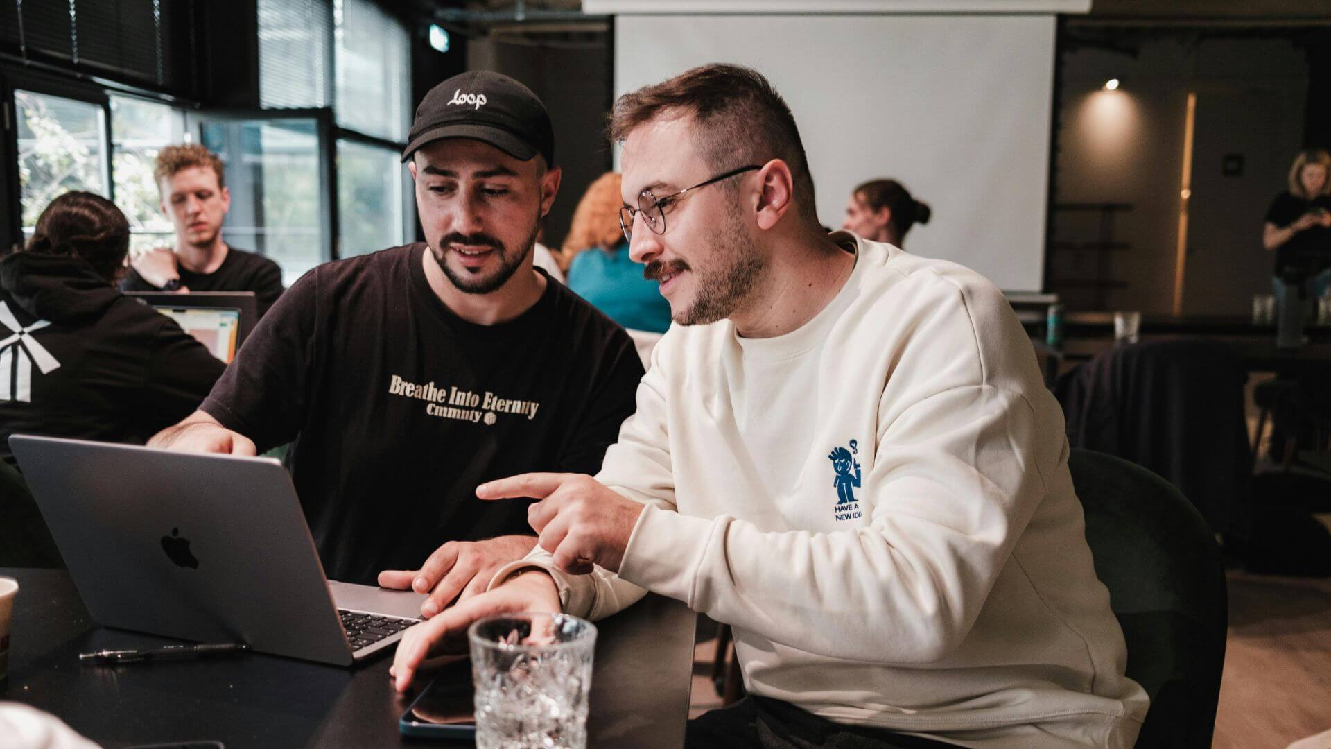 Dos jóvenes profesionales revisan una notebook y conversan sobre las acciones de una startup en un espacio de trabajo colaborativo.