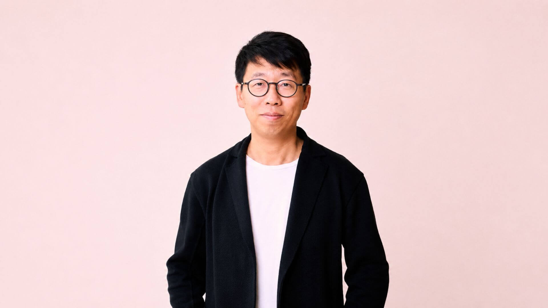 Retrato de un ejecutivo con anteojos y saco negro sobre fondo rosa, en una imagen corporativa de Airwallex.