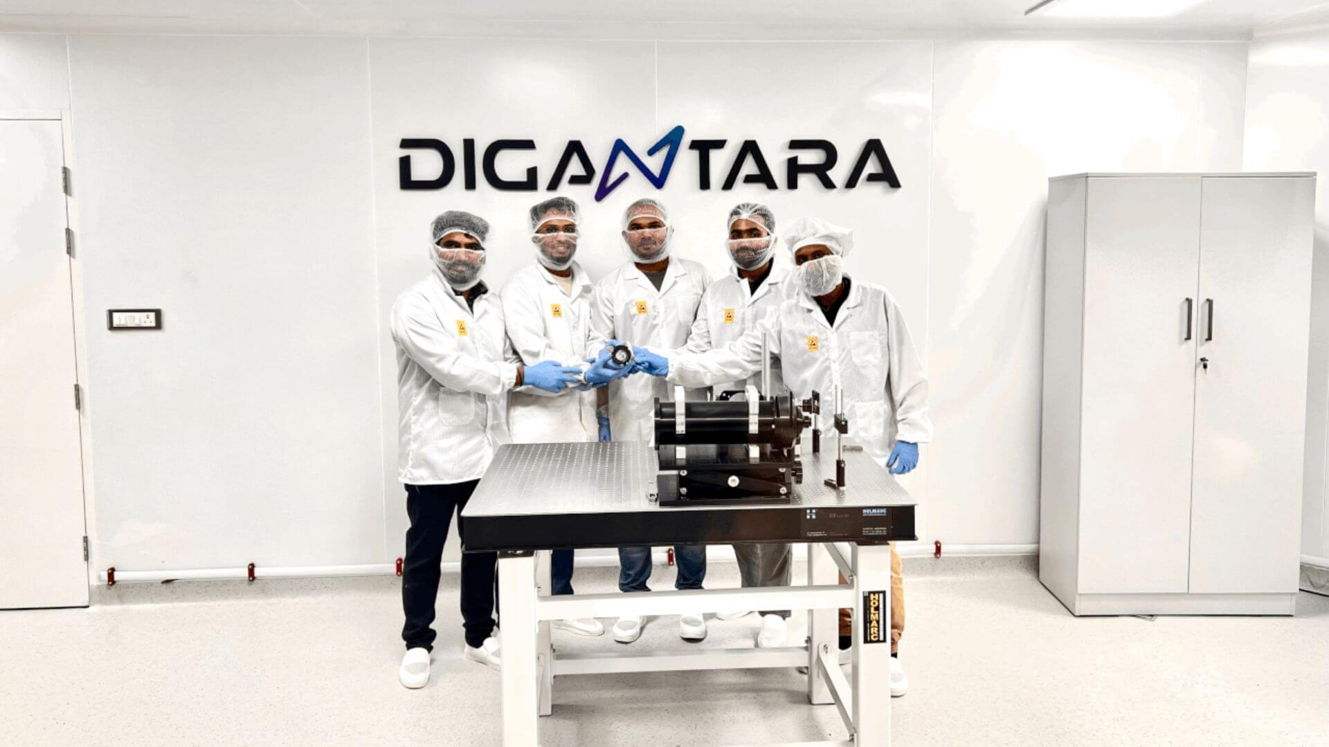 Cinco técnicos de Digantara con ropa de sala limpia exhiben un componente satelital junto a equipos de laboratorio.