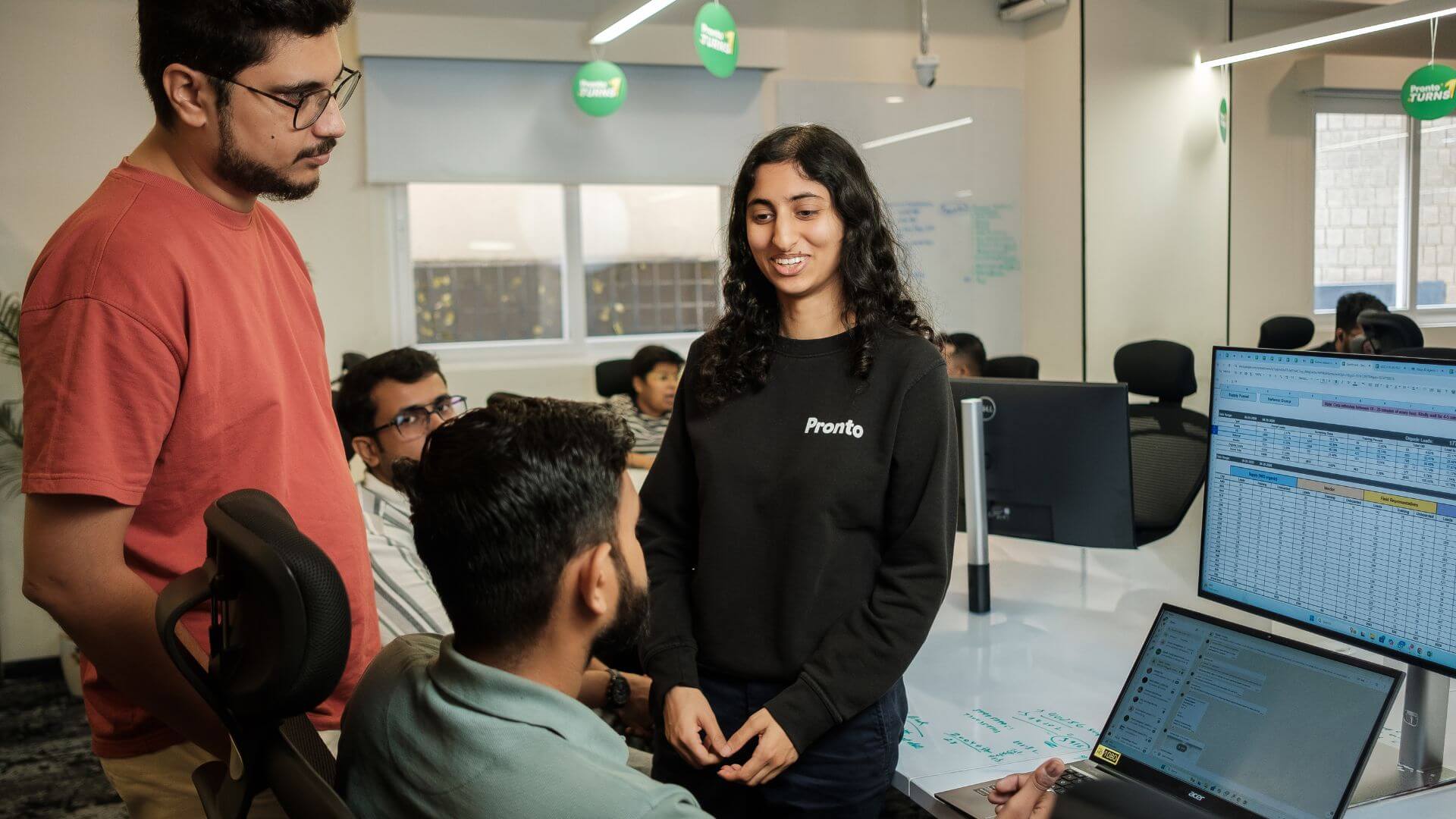 Integrantes del equipo de Pronto conversan junto a computadoras dentro de una oficina.