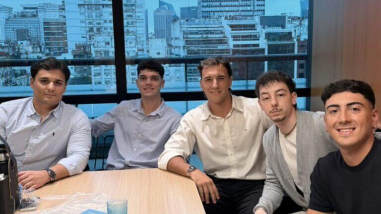 Cinco integrantes del equipo de Urbania posan en una oficina con edificios de la ciudad al fondo.