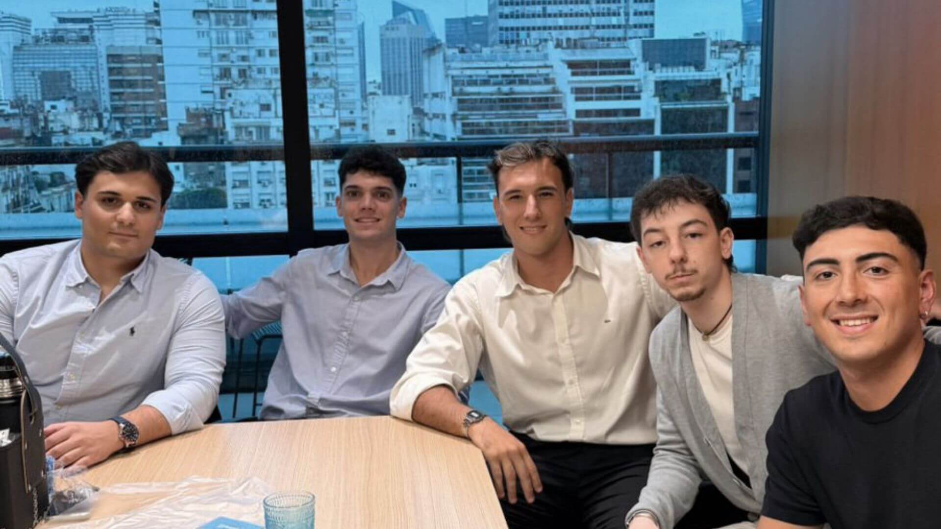 Cinco integrantes del equipo de Urbania posan en una oficina con edificios de la ciudad al fondo.