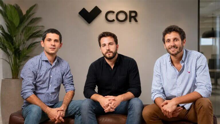 Tres integrantes del equipo de COR posan en una oficina frente al logotipo de la compañía tecnológica argentina.
