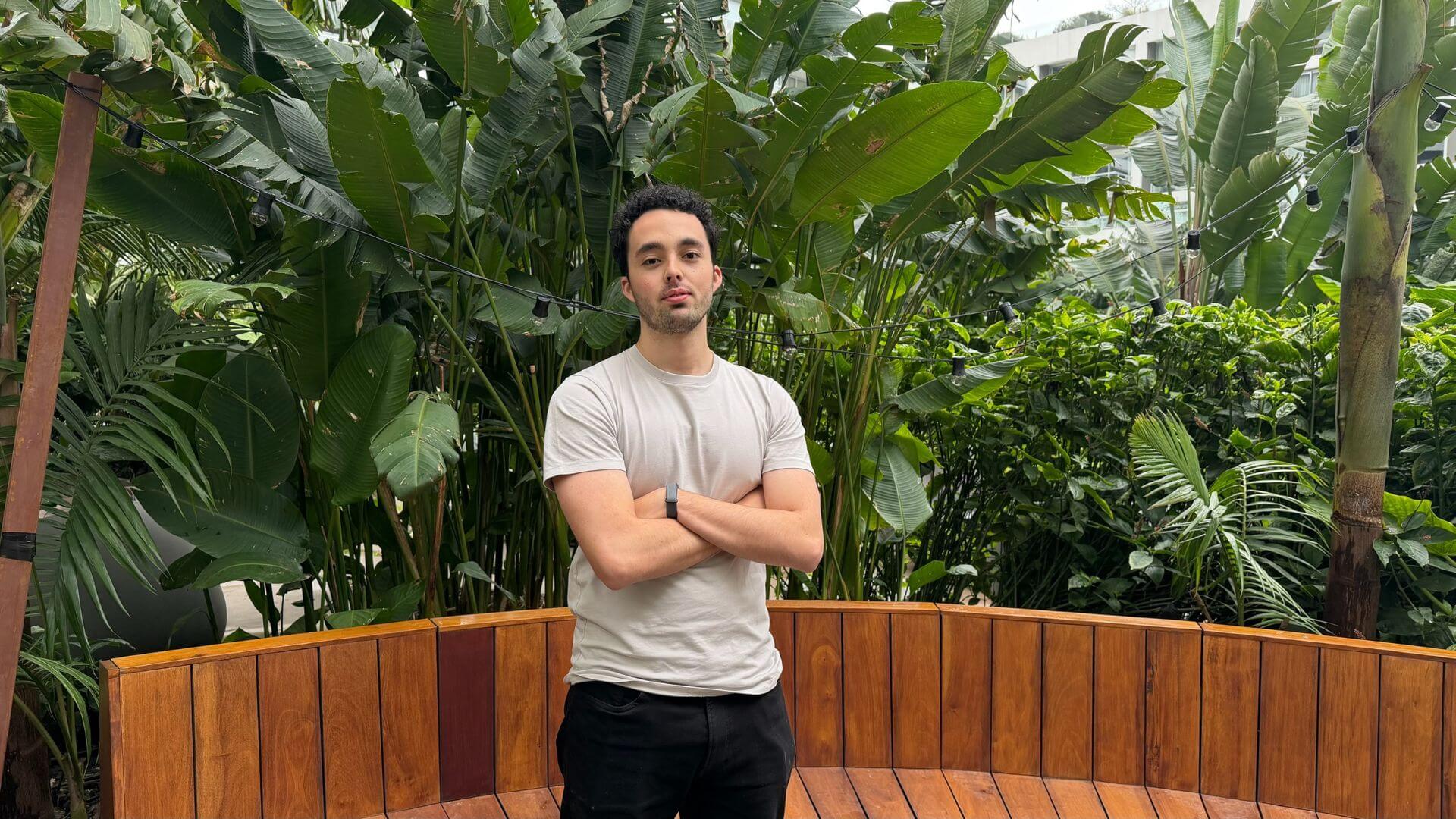 Joven emprendedor de pie frente a plantas tropicales, en una imagen vinculada con la historia de Plaude.