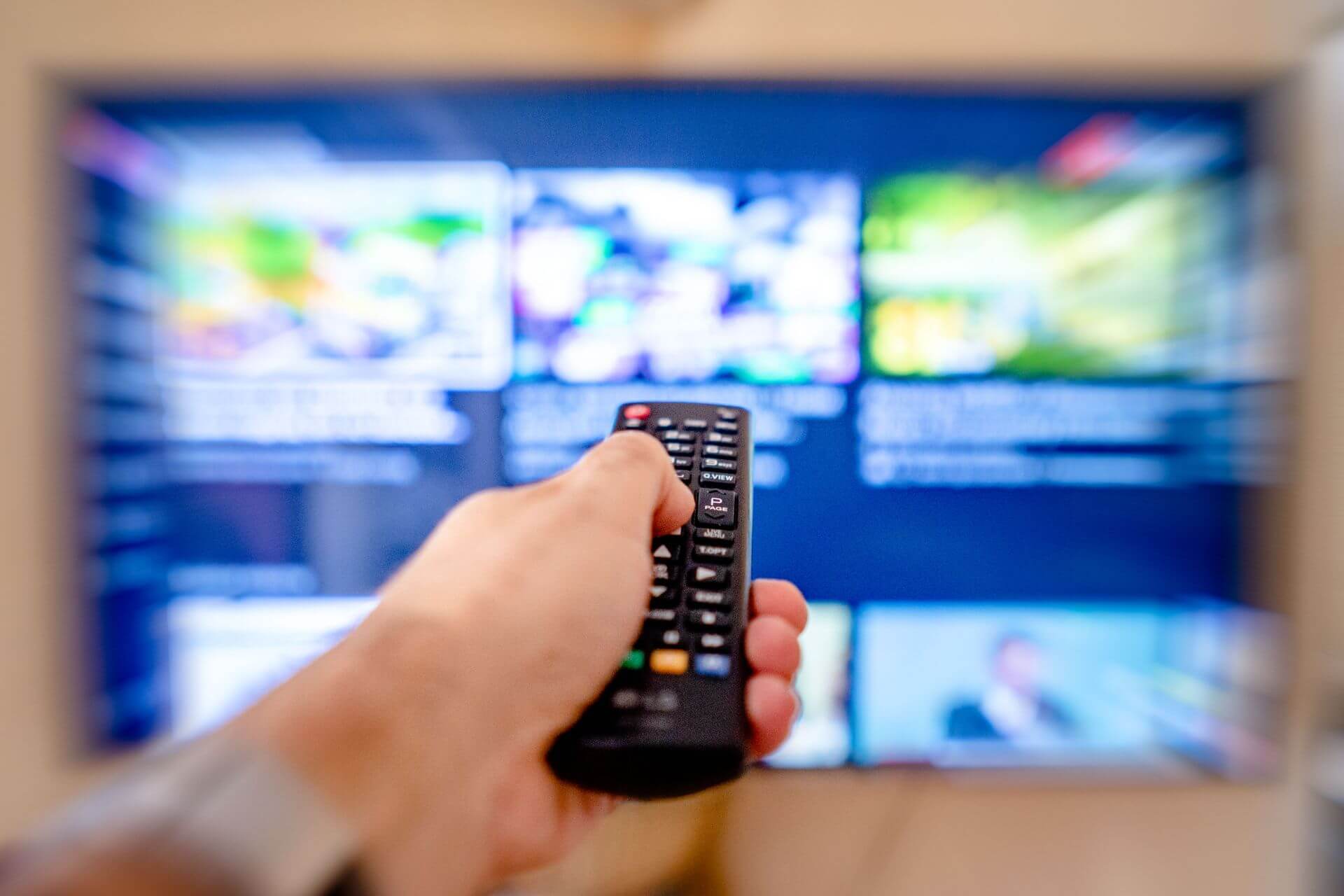 Mano con control remoto frente a una Smart TV que muestra un menú de contenidos, en una escena asociada al streaming en Argentina y al consumo audiovisual bajo demanda.
