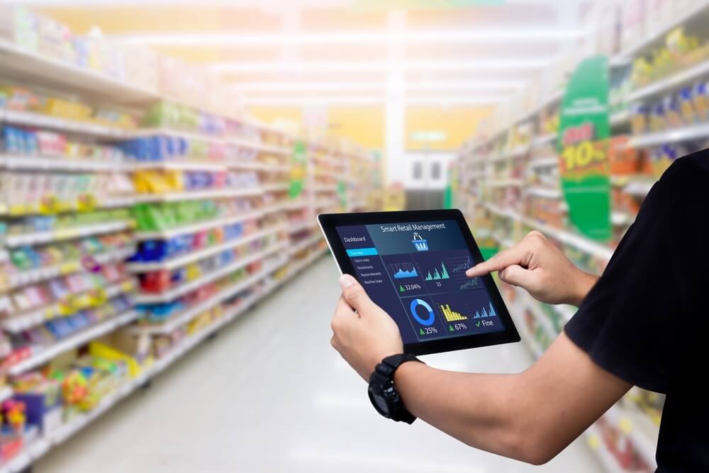 Trabajador consulta en una tablet datos de inventario en tiempo real dentro de un supermercado, una capacidad clave del comercio unificado.