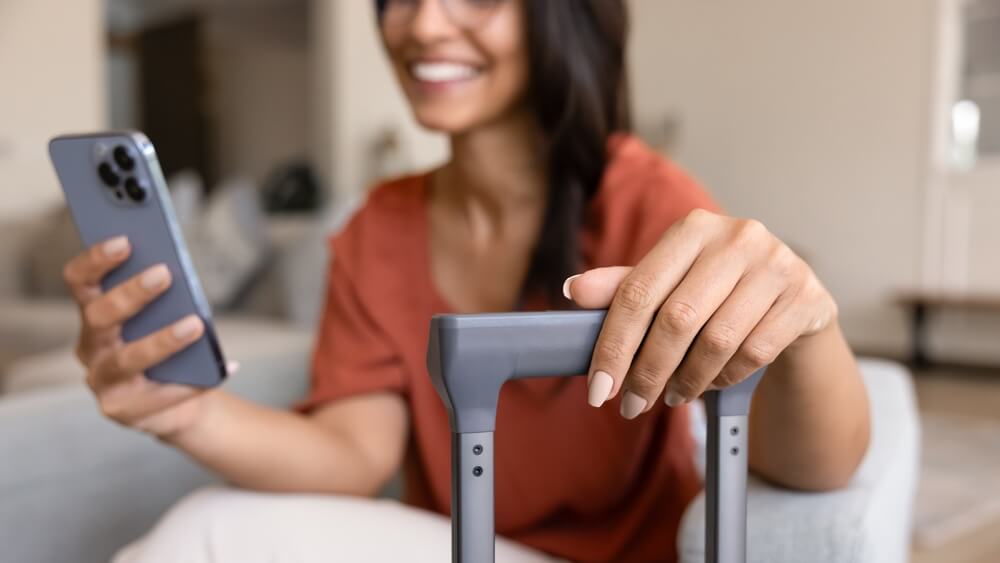 Huésped con valija consulta reseñas hoteleras en su teléfono dentro de una habitación.