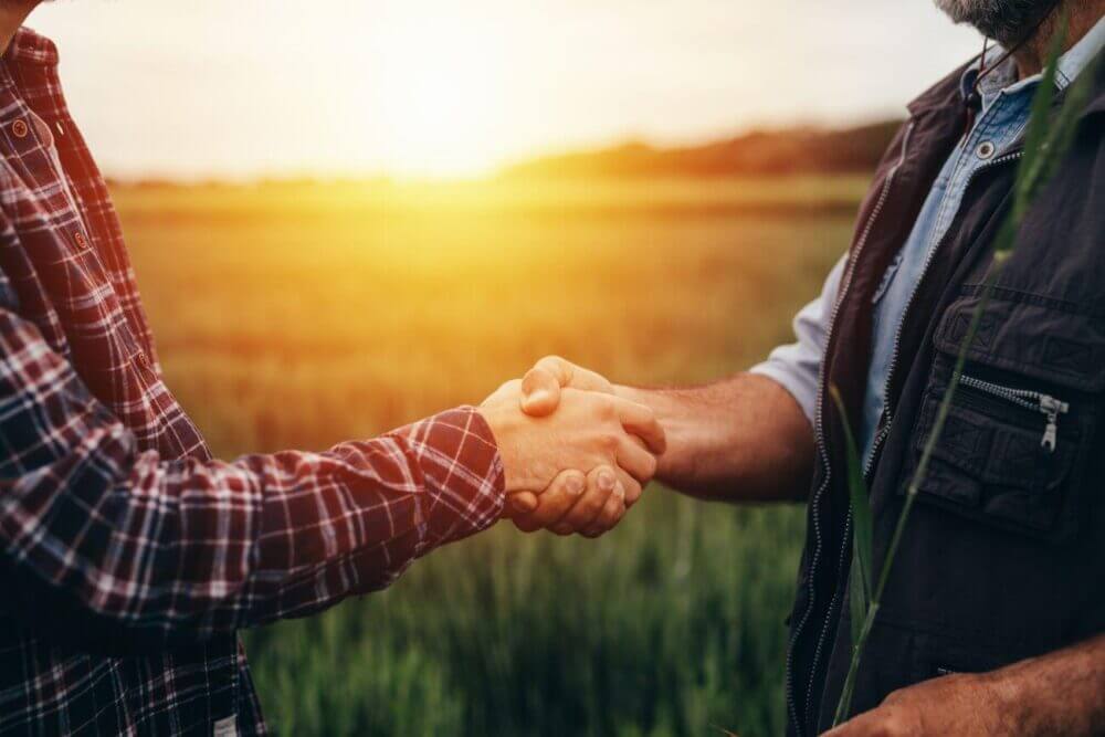 Dos productores se dan la mano en un campo, como representación de los acuerdos para compartir datos agropecuarios.
